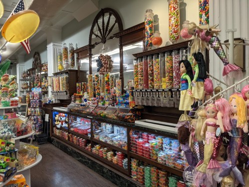 A colorful candy shop filled with jars of sweets, toys, and vibrant decorations along the walls.