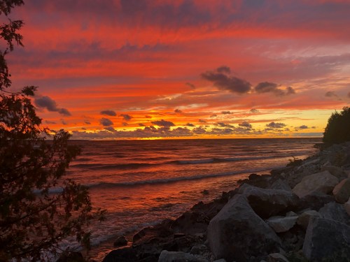 Vibrant sunset over the ocean, with colorful clouds reflecting on the water and rocky shoreline in the foreground.