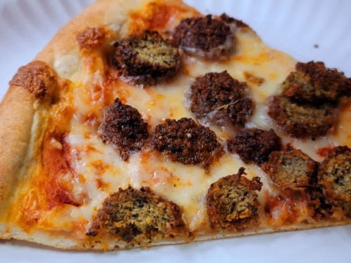 A slice of pizza topped with melted cheese and pieces of crispy, seasoned sausage.