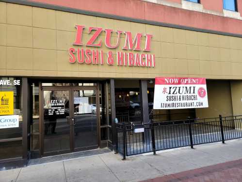 Exterior of Izumi Sushi & Hibachi restaurant with a "Now Open" banner displayed.