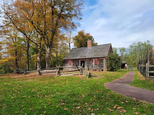 A rustic wooden cabin surrounded by autumn trees and a grassy area, with a path leading towards it.