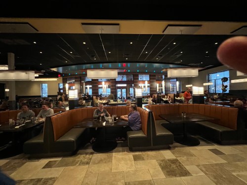 A busy restaurant interior with booths and tables filled with diners, featuring modern decor and soft lighting.
