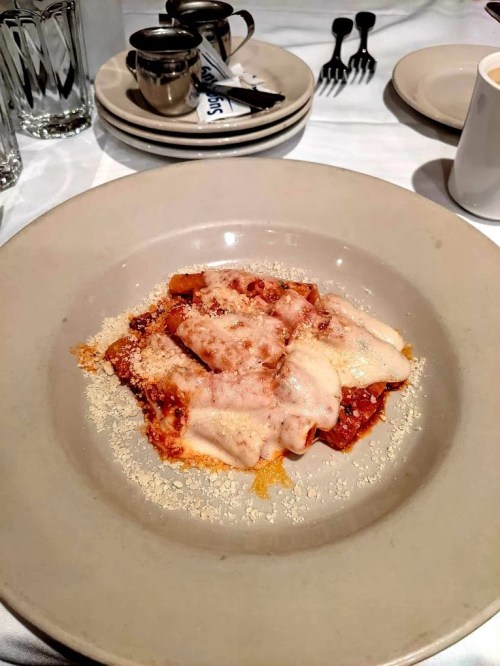 A plate of baked pasta topped with melted cheese and sprinkled with grated cheese, served on a white tablecloth.