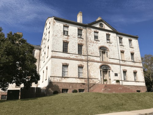Historic brick building with a white facade, large windows, and a grassy area in front under a clear blue sky.