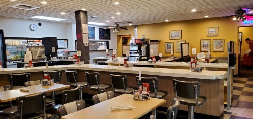 A cozy diner interior with a long counter, tables, and retro decor, featuring condiments on each table.