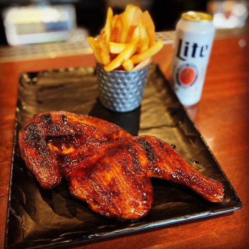 Grilled chicken wings glazed with sauce, served with fries in a cup and a can of beer on the side.