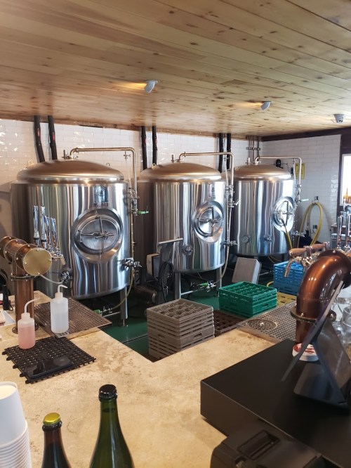 Three large stainless steel brewing tanks in a brewery, with various tools and containers on a countertop.