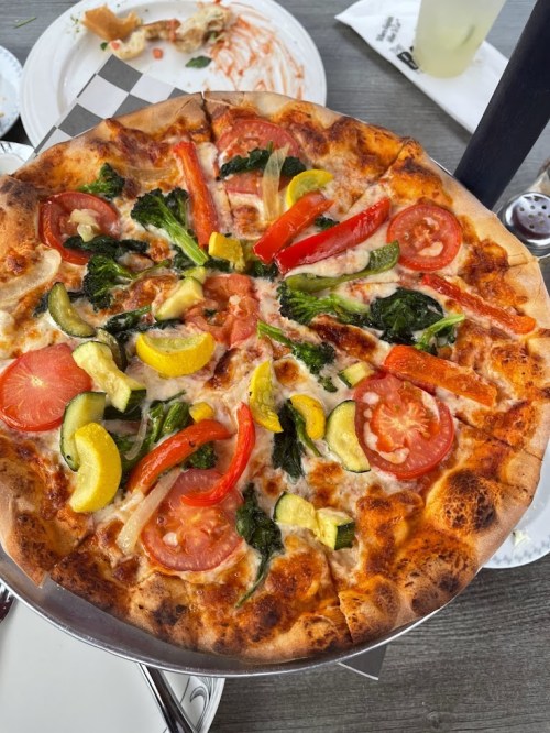 A freshly baked vegetable pizza topped with tomatoes, bell peppers, zucchini, and broccoli on a silver serving tray.