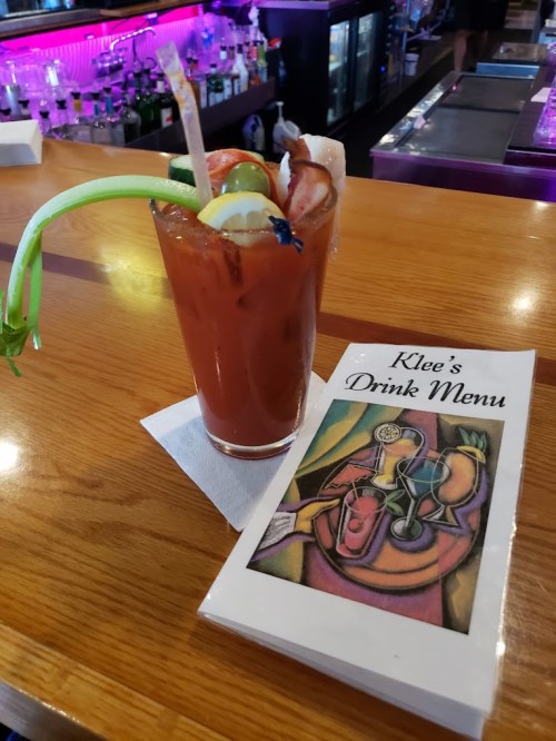 A colorful cocktail with a celery garnish next to a drink menu on a wooden bar.