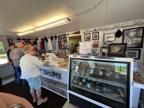 A small shop interior with customers at the counter, displaying framed photos and a glass case of products.