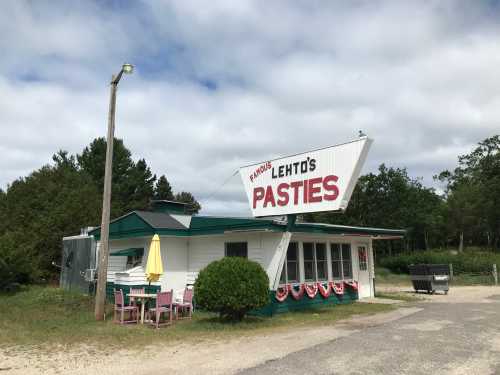 A quaint roadside eatery with a large sign reading "Lehto's Pasties," surrounded by greenery and picnic tables.