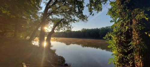 A serene river scene at sunrise, with mist rising from the water and trees framing the view.