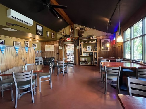 Cozy restaurant interior with wooden walls, tables, and decor including mounted animal heads and framed photos.