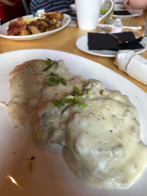 A plate of biscuits smothered in creamy gravy, garnished with green onions, on a dining table.