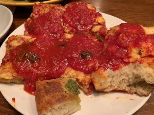 A plate of bread topped with a thick layer of red sauce and green peppers, with a piece of bread broken off.