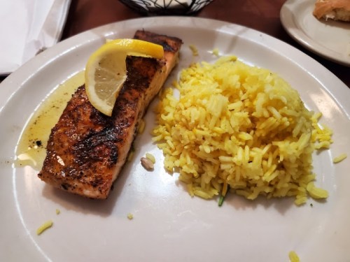 Grilled salmon fillet with a lemon slice, served alongside yellow rice on a white plate.
