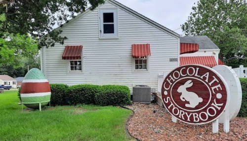 A white house with red awnings and a large sign reading "Chocolate Storybook," featuring a bunny logo and a colorful egg.
