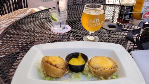 A plate with two cheese-filled fried appetizers, a small cup of mustard, a glass of beer, and a drink on a table.