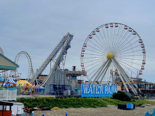 A vibrant amusement park featuring a Ferris wheel, roller coaster, and a water park sign against a cloudy sky.