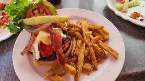 A plate featuring a burger with lettuce, tomato, bacon, and pickles, served with a side of crispy fries.