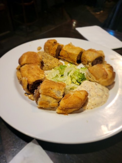 A plate of savory pastries filled with meat, surrounded by lettuce and dipping sauces.