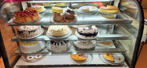 A display case filled with various cakes, including cheesecakes, fruit tarts, and chocolate desserts.