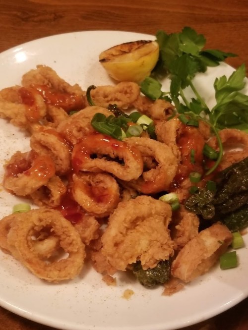 A plate of crispy fried calamari drizzled with sauce, garnished with green onions and a lemon wedge.