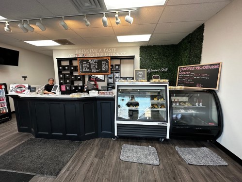 A cozy café interior featuring a service counter, display case, and menu boards, with a barista at work.