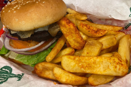 A sesame seed bun burger with lettuce, tomato, onion, and pickles, served with seasoned potato wedges.