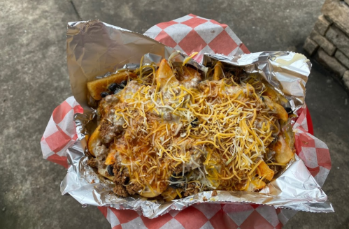 A foil-wrapped tray of loaded nachos topped with melted cheese, ground beef, and various toppings on a checkered paper.
