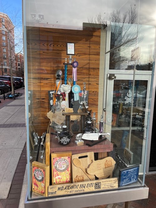 Display case showcasing various awards, trophies, and memorabilia related to BBQ and cooking competitions.