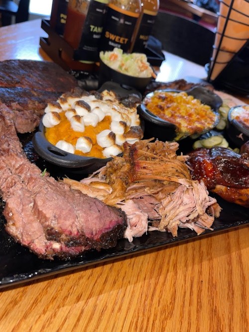 A platter of assorted meats, including brisket and pulled pork, accompanied by sides like sweet potatoes and coleslaw.