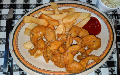 A plate of golden fried shrimp with French fries and a side of ketchup on a checkered tablecloth.