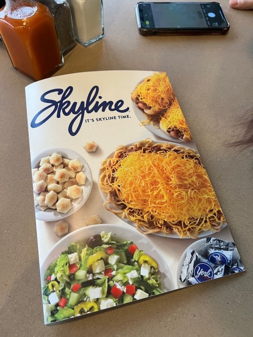 A menu for Skyline featuring dishes with cheese, salad, and crackers on a table with condiments and a phone.