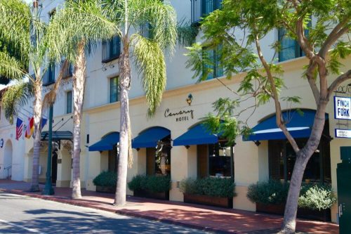 Exterior of the Canary Hotel, featuring palm trees, blue awnings, and a welcoming entrance.