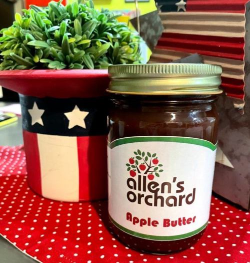 A jar of apple butter from Allen's Orchard next to a decorative plant and a red, white, and blue themed pot.