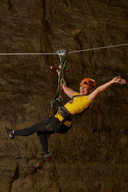 A person in a yellow shirt and helmet joyfully zip-lining across a rocky cave.