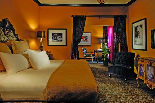 Cozy hotel room with a large bed, elegant decor, dark curtains, and a small seating area with a plant.