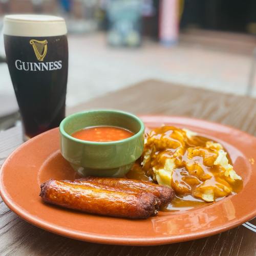 A plate with sausages, gravy-covered fries, and a bowl of beans, alongside a pint of Guinness.