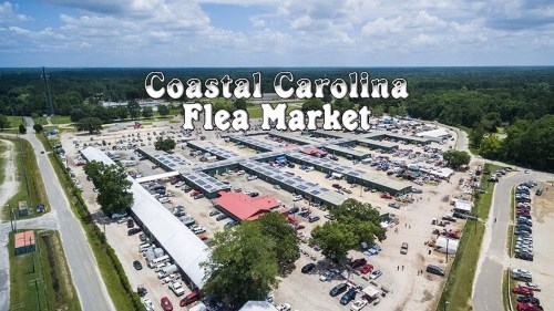 Aerial view of Coastal Carolina Flea Market, featuring numerous stalls, cars, and a green landscape under a blue sky.