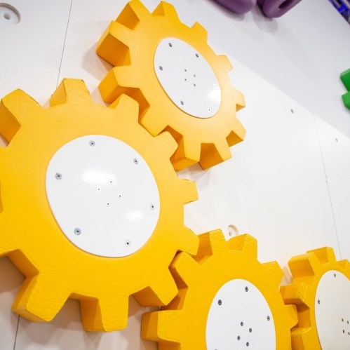 Colorful yellow gear shapes mounted on a white wall, part of a playful, interactive display.