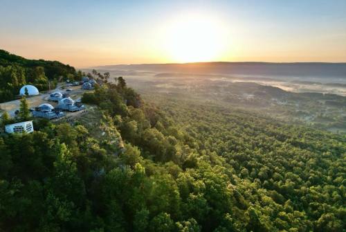 Aerial view of lush green hills and valleys at sunrise, with domed structures nestled among the trees.