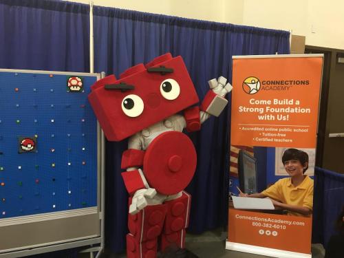 A large red robot mascot stands next to a banner for Connections Academy, featuring a smiling child and educational info.