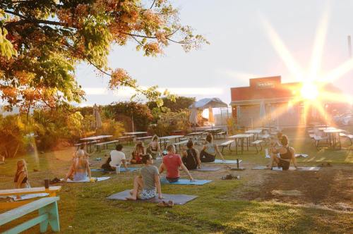 A group of people practicing yoga outdoors at sunset, with tables and a building in the background.