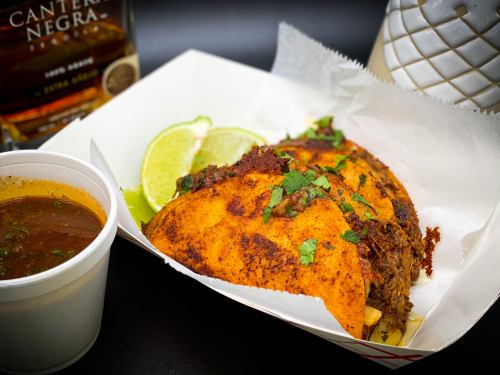 Three crispy tacos filled with meat, garnished with cilantro, served with lime wedges and a cup of broth.