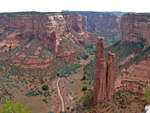 A vast canyon landscape featuring towering rock formations, green vegetation, and a winding river below.