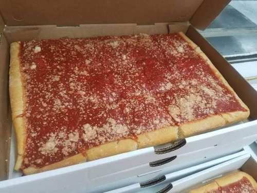 A rectangular pizza with a thick crust, topped with red sauce and sprinkled with grated cheese, in a pizza box.