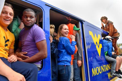 A group of people smiling and enjoying a ride in a blue train, with one person dressed in a costume outside.