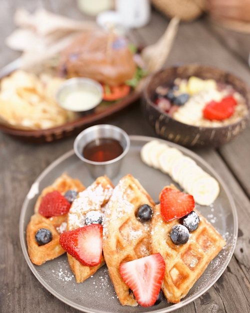 A plate of waffles topped with strawberries and blueberries, served with syrup and banana slices on a wooden table.