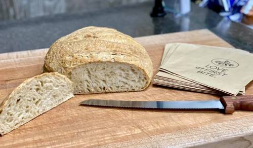 A freshly baked loaf of bread on a wooden cutting board, with a serrated knife and paper napkins nearby.